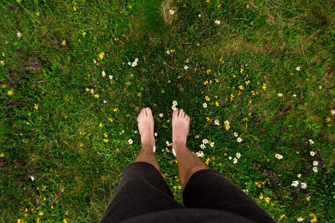 A top-down view of bare feet standing on grass scattered with small wildflowers.