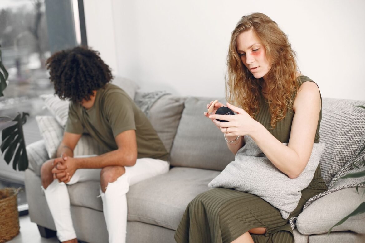 A couple sitting at opposite ends of a sofa, each turned away and lost in thought.