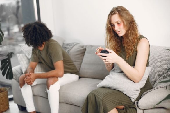 A couple sitting at opposite ends of a sofa, each turned away and lost in thought.