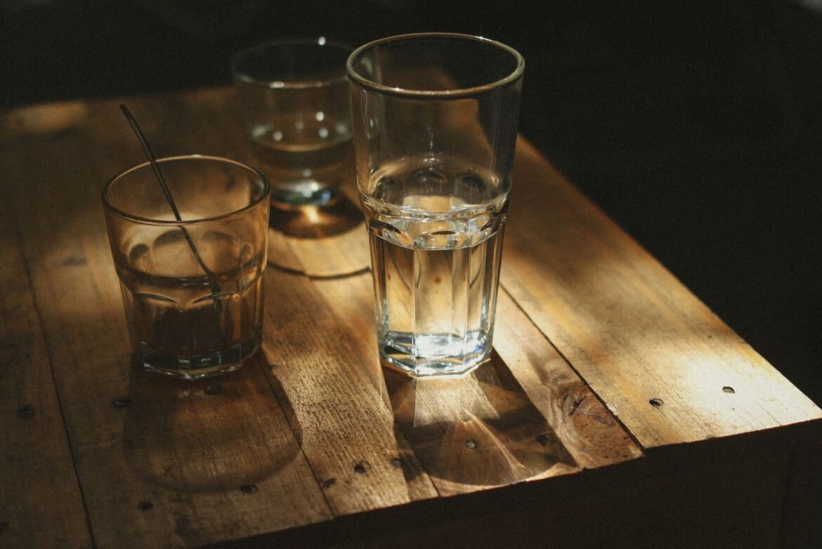 Empty drinking glasses on a wooden table, casting long shadows in low light.
