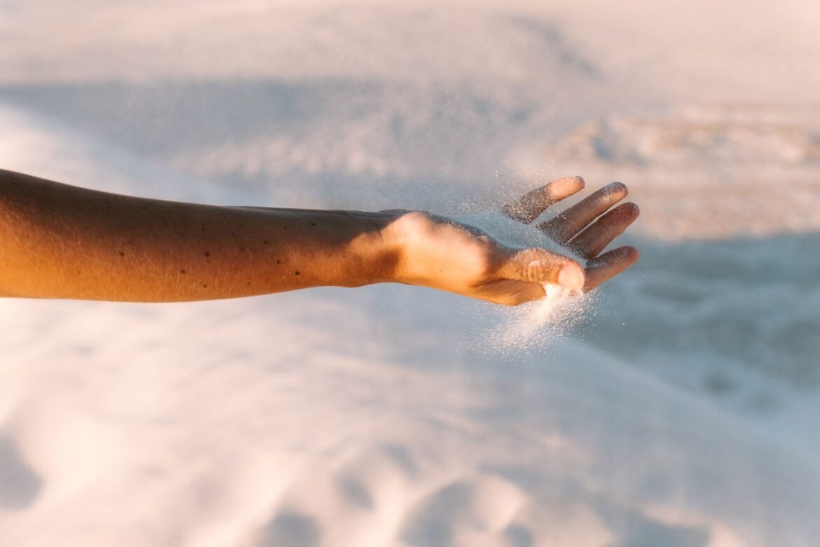 A close-up of an open hand letting dry sand run out through the fingers at sunset.