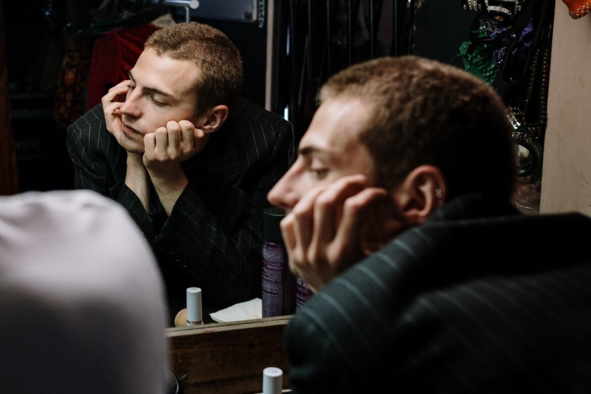 A man stands looking at his own reflection in a mirror.