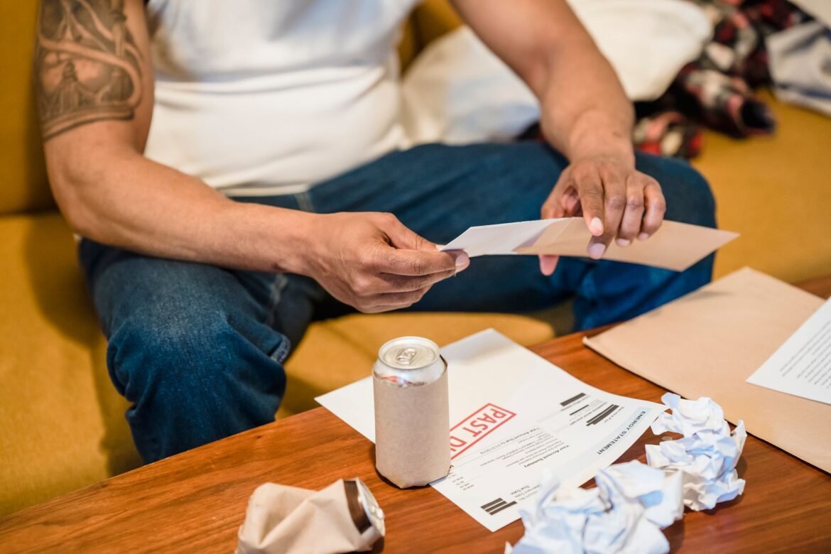 A man sitting on a couch sorting through opened envelopes and paperwork.