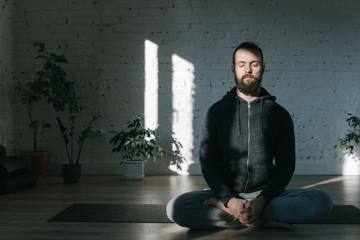 A man sitting cross-legged on the floor indoors with his eyes closed, meditating.