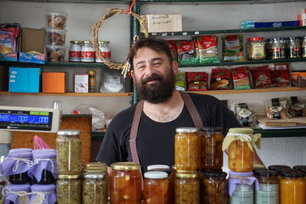 A shopkeeper standing behind shelves stacked with jars of homemade preserves.