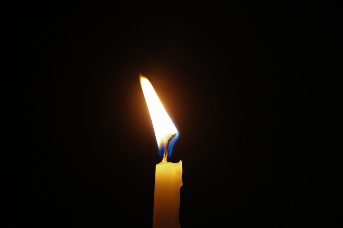 A single candle flame burning against a dark background.