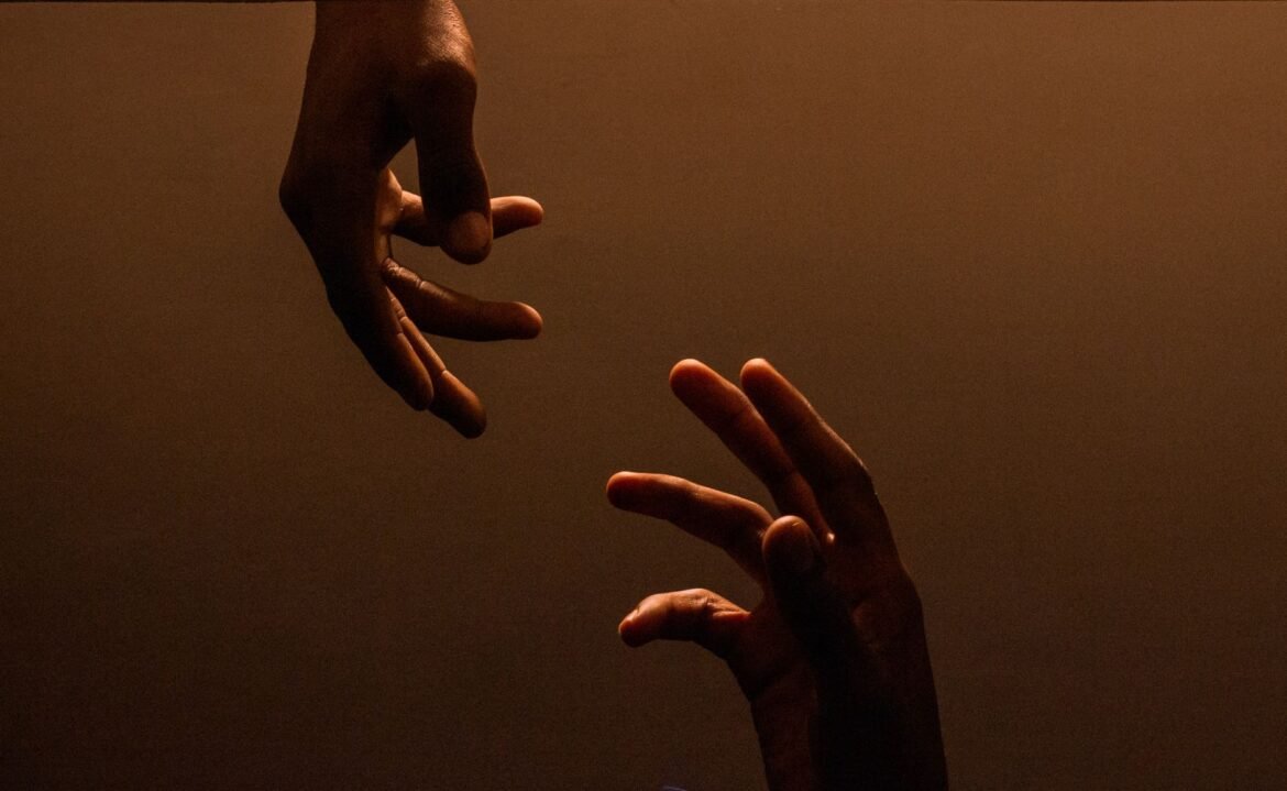 Two hands reaching toward each other against a warm, dark background.