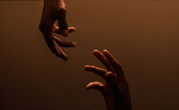 Two hands reaching toward each other against a warm, dark background.