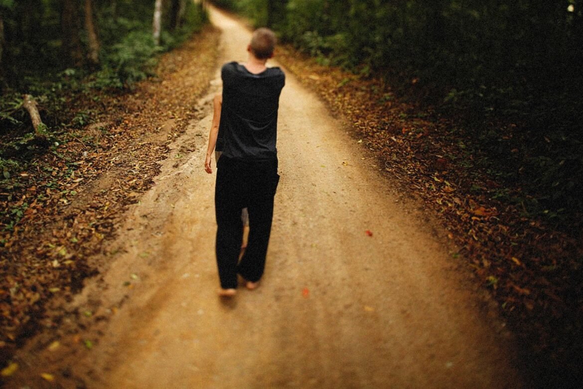 A person walking barefoot along a dirt path through woodland.