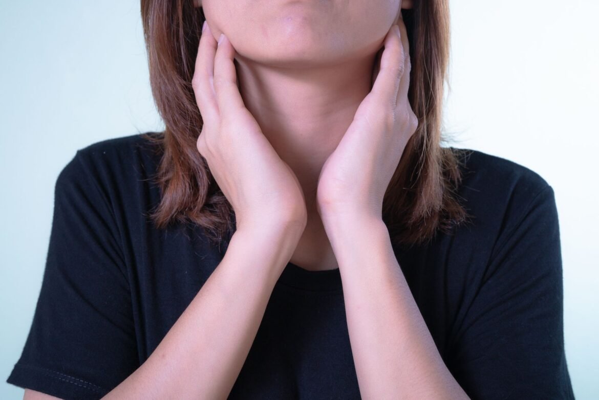 A close-up of a woman resting her hand against the front of her throat.
