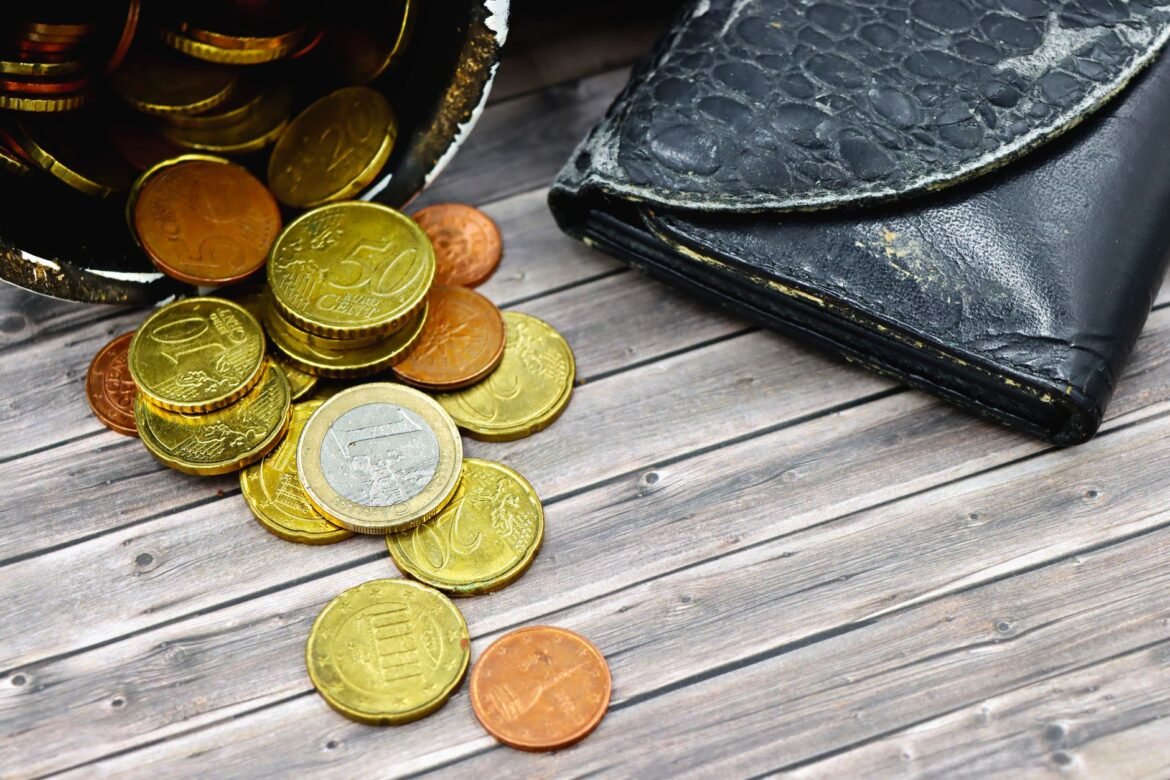 A worn leather wallet lying open on a wooden surface with a few coins scattered beside it.