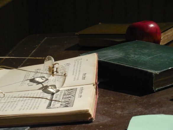 Old hardback books and a pair of reading glasses on a desk