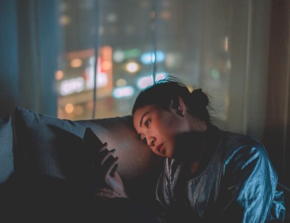 A person looking at their phone alone in a dimly lit room