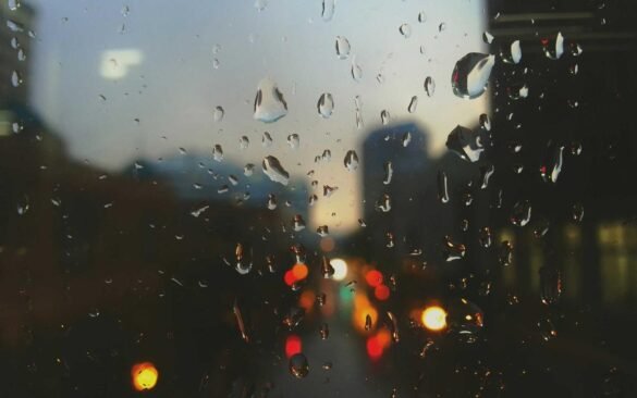 Raindrops on a dark window with blurred lights beyond