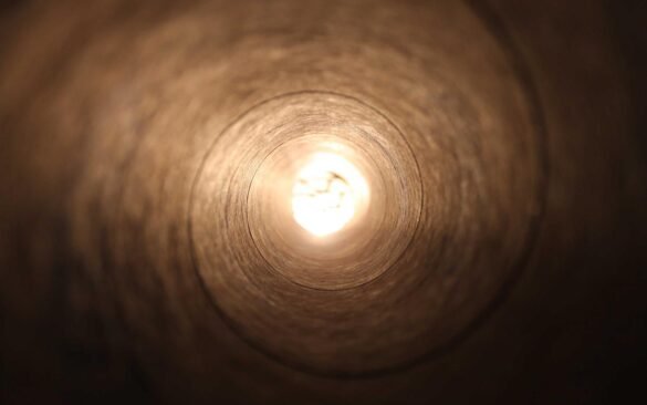 A dark tunnel opening toward bright light at its far end